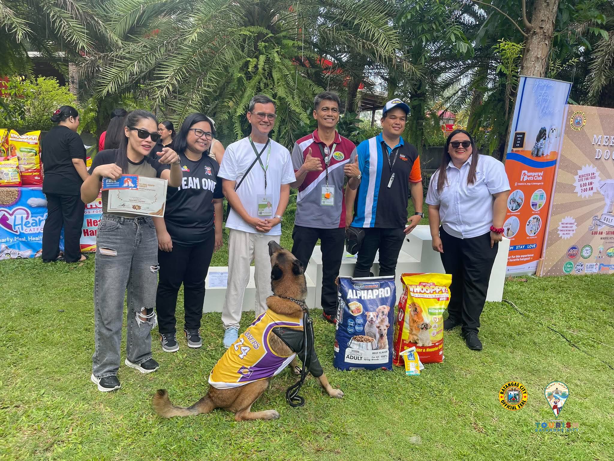 A participant holding a certificate beside her dog and sacks of dog food