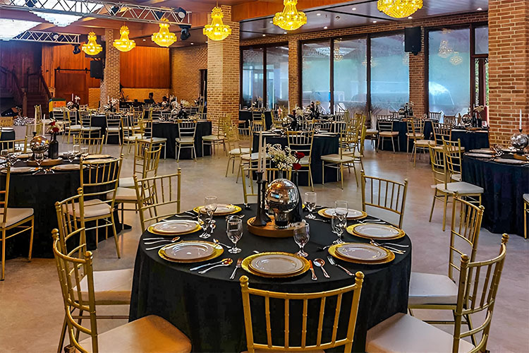 Round tables set in black and gold inside the event hall at Rancho Blanco